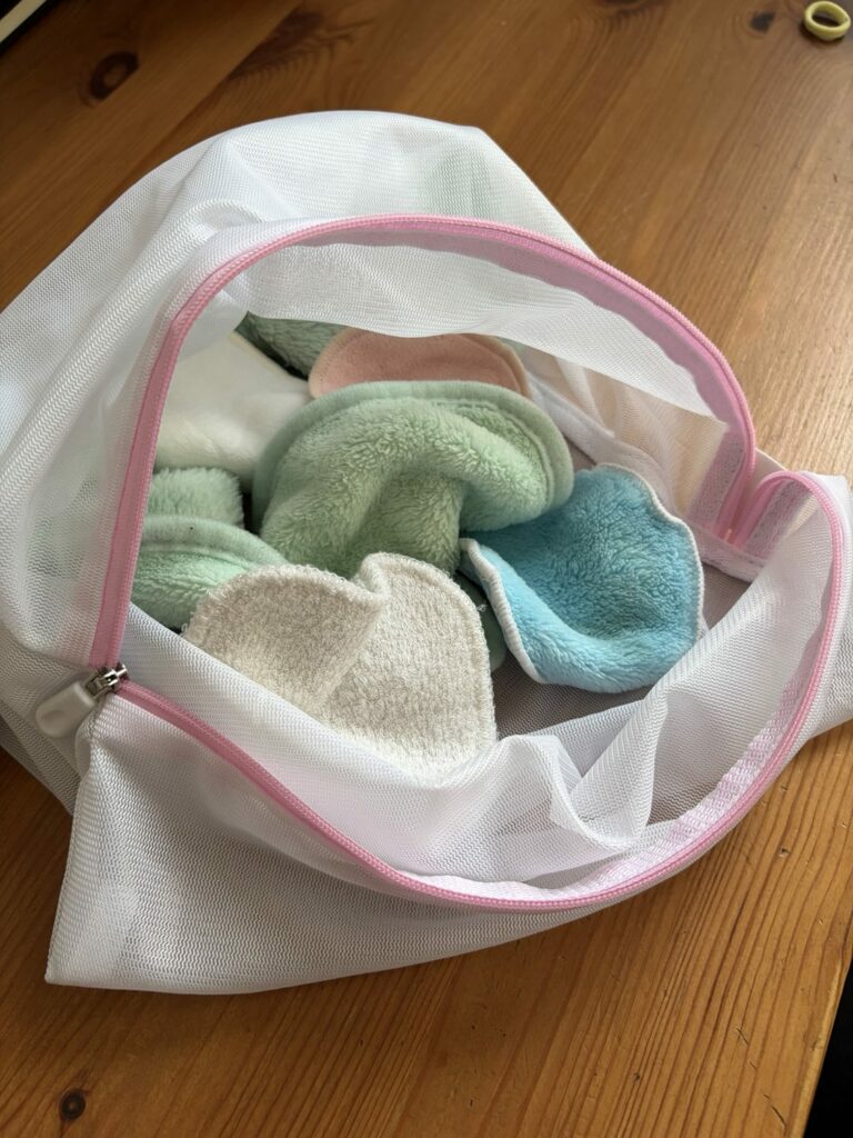 Filet blanc à fermeture rose contenant des lingettes lavables vertes, bleues et écrues.